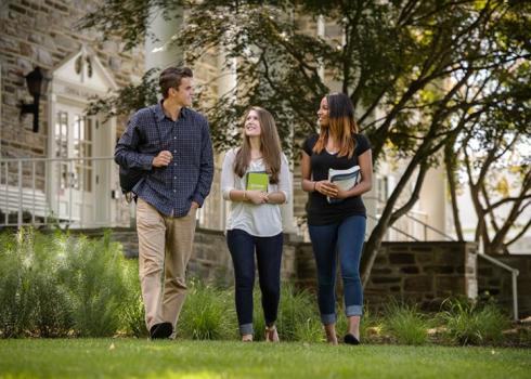 Three college students walk across the quad, away from an academic building.