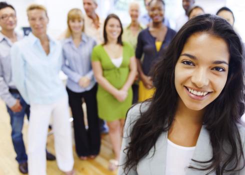 Ready for their team selfie, a group of people gather behind a young woman in business attire.