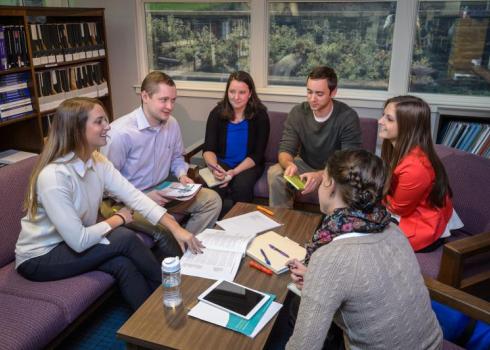 Gathered around a small table in the library, a group of college students study together.