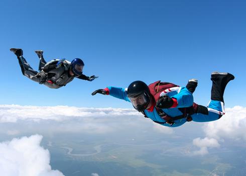 A pair of skydivers during freefall above the clouds. A river meanders in the distance.