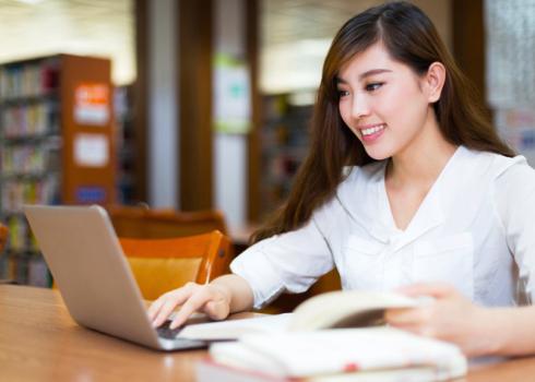 In a library, a young Asian woman uses a laptop
