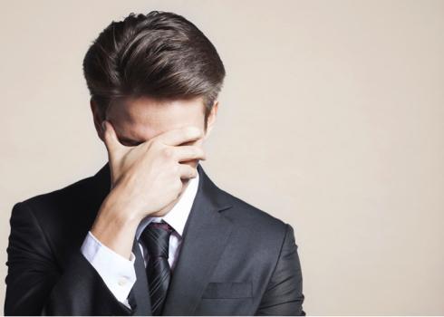 A young man in a business suit covers his face with his hand in shame